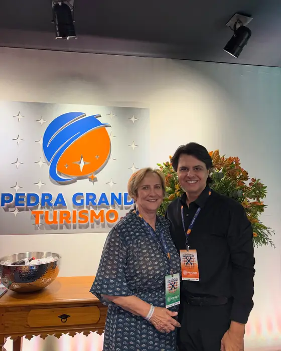 Duas pessoas da Pedra Grande com crachá, na frente do logotipo iluminado da agência.